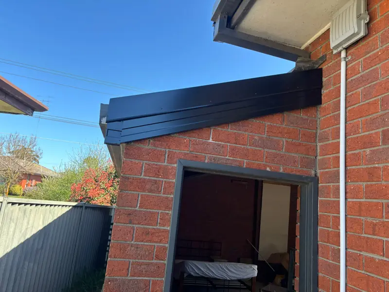 New black metal flashing along a sloping roof edge where it meets a brick wall