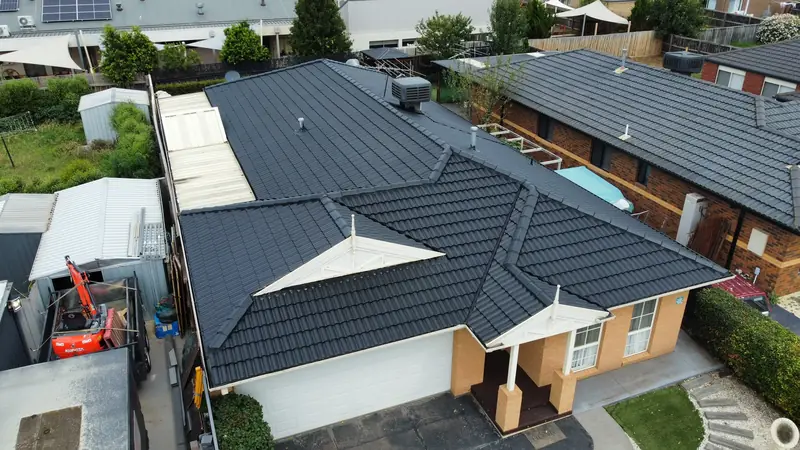 Charcoal painted tile roof on a brick home with white gable trim, aerial view
