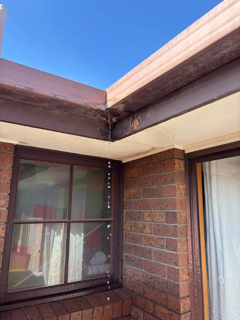 Water running out of a rusted gutter corner joint above a window