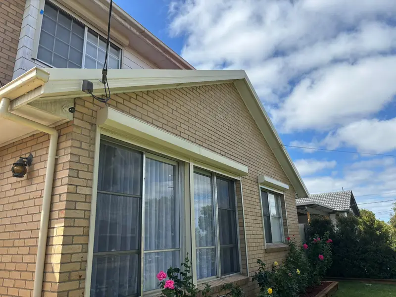 Cream gutters, fascia and downpipe on a gable-front brick home