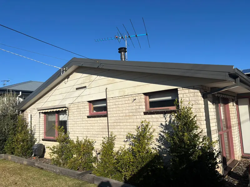 Cream brick home with grey gutters and fascia and a TV antenna on the roof