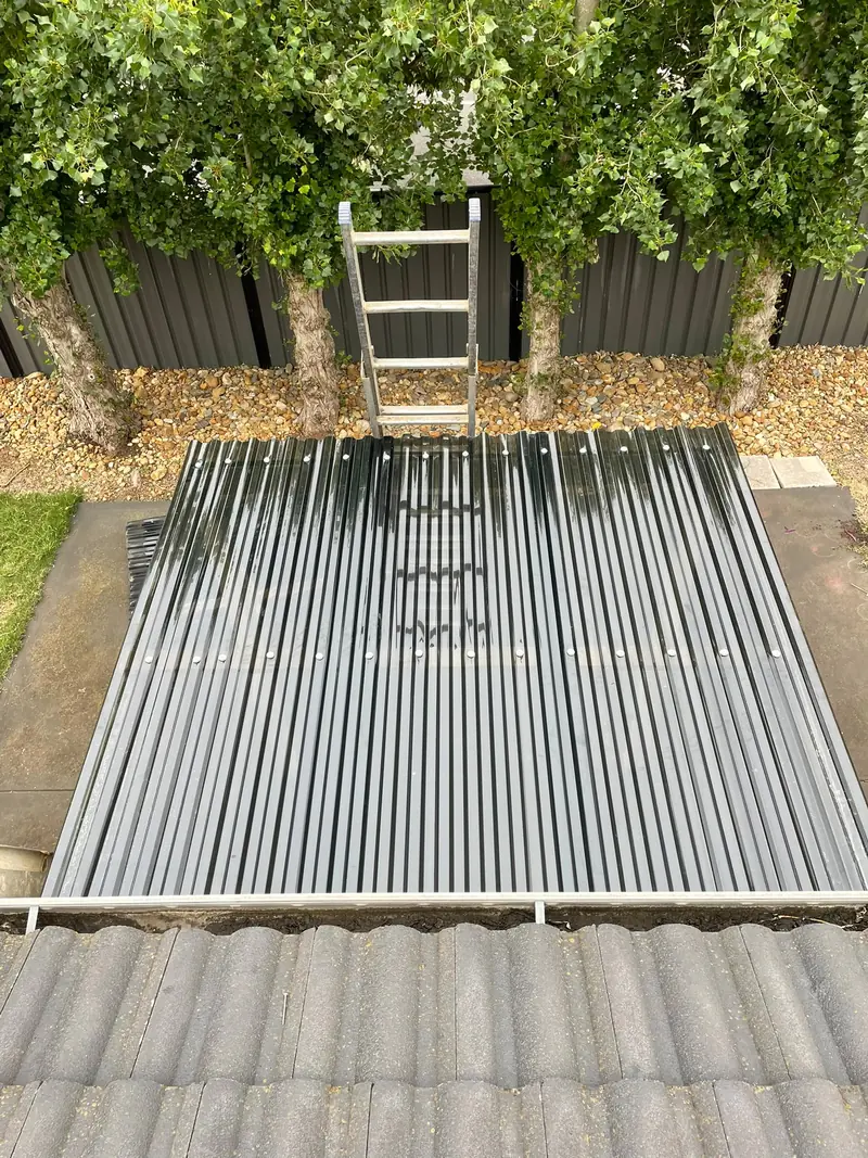 New corrugated grey roof sheeting fixed on a patio beside a tile roof
