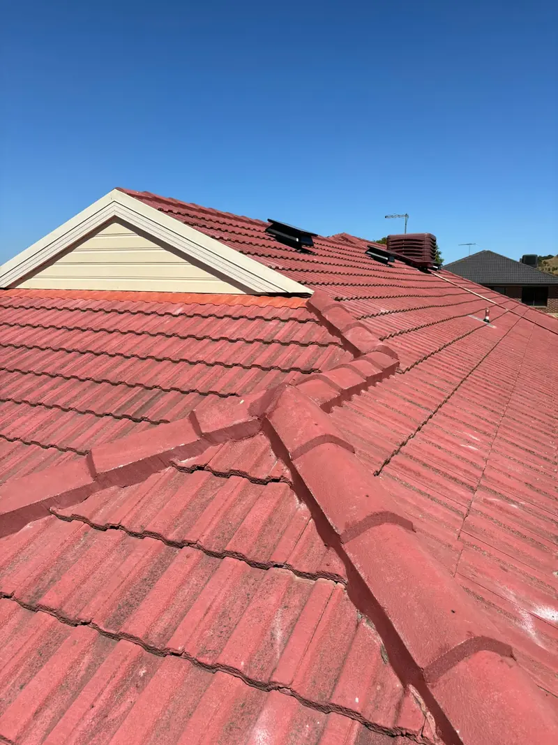 Red tile roof with a cream gable and roof vents under a clear sky