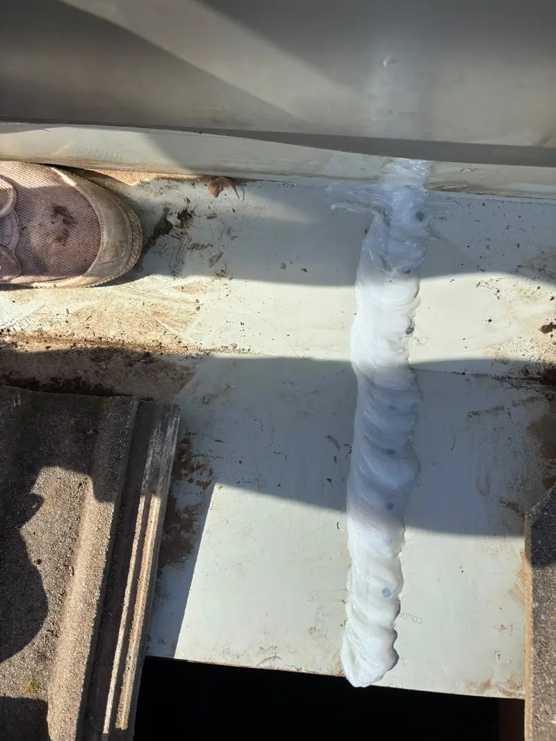 Sealant bead over the fixings of a metal flashing next to a tile roof